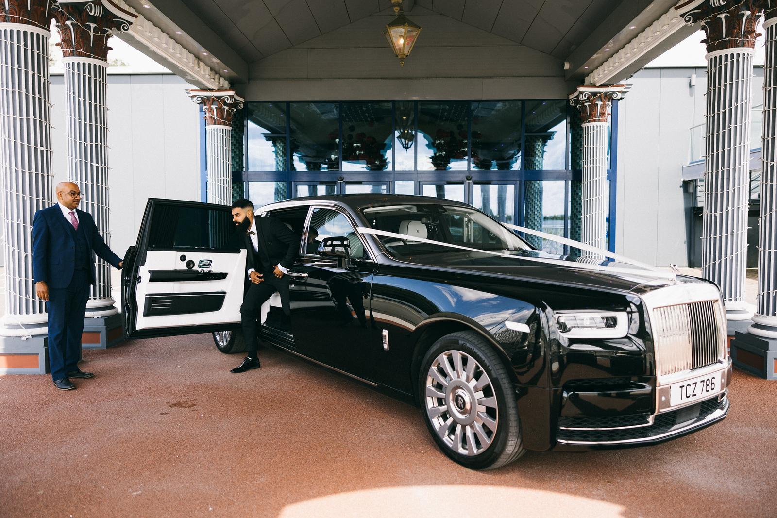 Man in suit exiting a luxury vehicle while a chauffeur is holding the door open